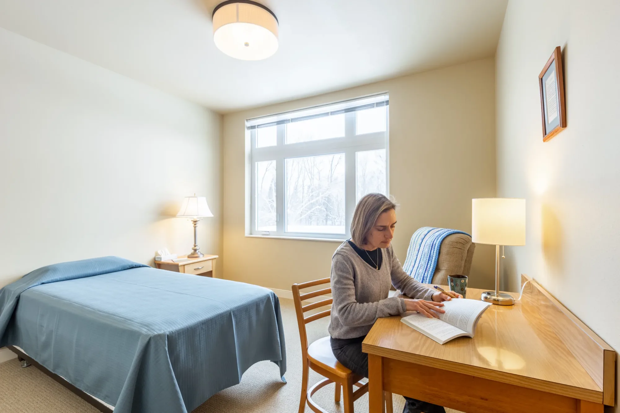 a woman sits reading quietly in a private bedroom at a spiritual retreat center