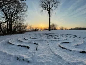 contemplative outdoor labyrinth covered in snow with trees and sunrise