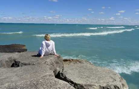 woman sits in contemplation on breakwater rocks on Lake Michigan