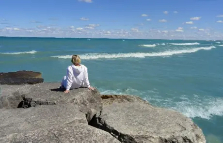 woman sits in contemplation on breakwater rocks on Lake Michigan while on a spiritual retreat
